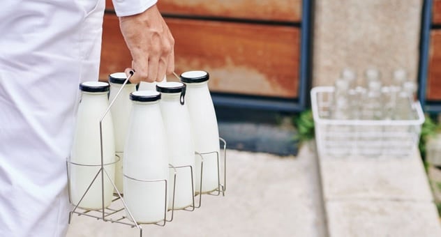hand holds mini-crate of six old-fashioned milk bottles near front doorstep