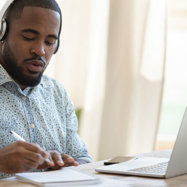 Focused man takes handwritten notes while working on laptop