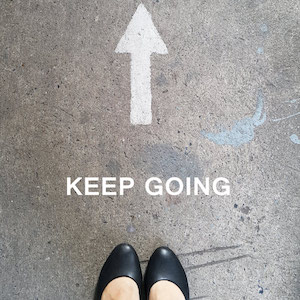 Feet on a pavement that has an arrow and 'keep going' painted on it