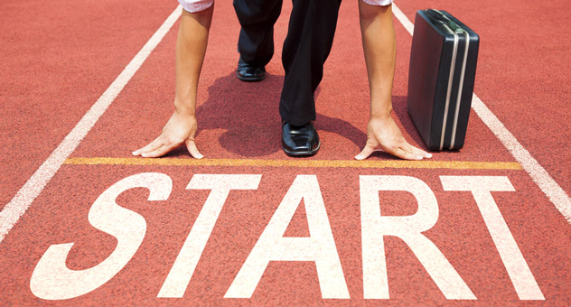 A business man with a suitcase crouching down at the starting line of a red race track. The word 'start' is large in white capital letters at the starting line.