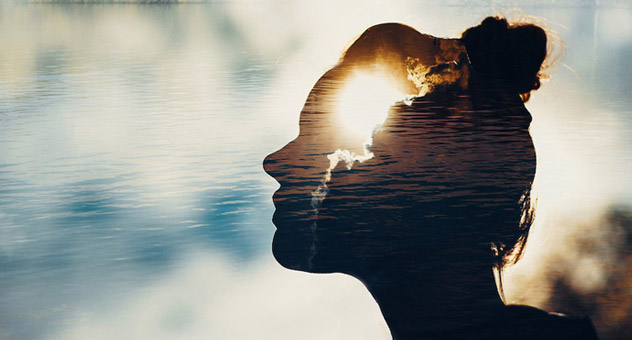 The profile of a woman's head set against a background with clouds, water and sunlight.