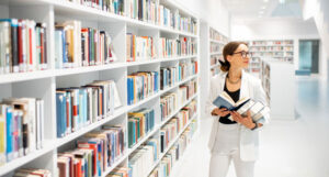 A woman standing in a library with an open book in her hand.