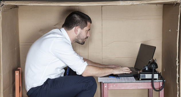 A man sitting at a desk, crammed into a large cardboard box.