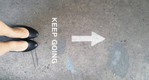 Top view of feet with an arrow and the words 'keep going' written on the floor in front of them.