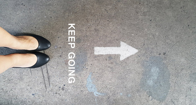 Top view of feet with an arrow and the words 'keep going' written on the floor in front of them.