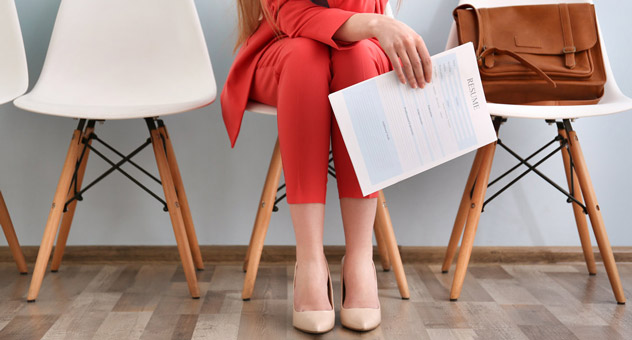 A job applicant sitting in a waiting area, holding her resume.
