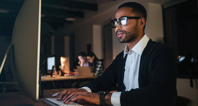 A man with glasses on sitting at his computer, typing.