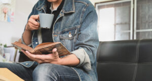 A man holding a coffee in one hand while reading a book.