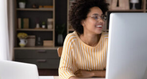 A woman in a yellow and white striped shirt sitting at her computer, smiling at the screen.