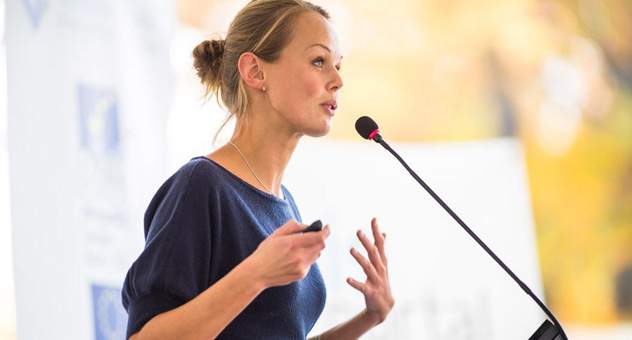 A woman at a microphone giving a presentation.