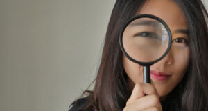 Woman holding a magnifying glass up to her eye.