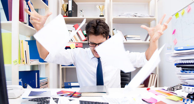 Office worker at messy desk throws papers in air and screams