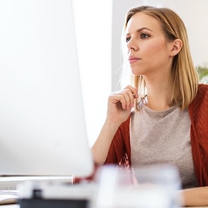 Thoughtful person sitting at desk and looking at computer screen