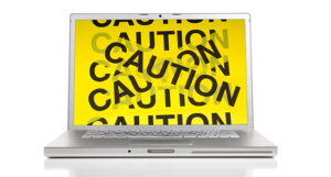 laptop with screen covered in yellow tape reading 'Caution'