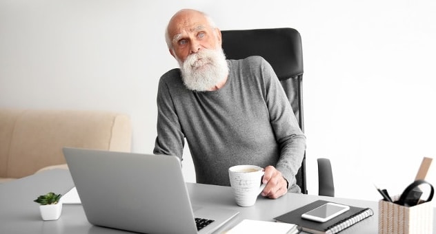 Elderly looking bearded person looking thoughtful at laptop
